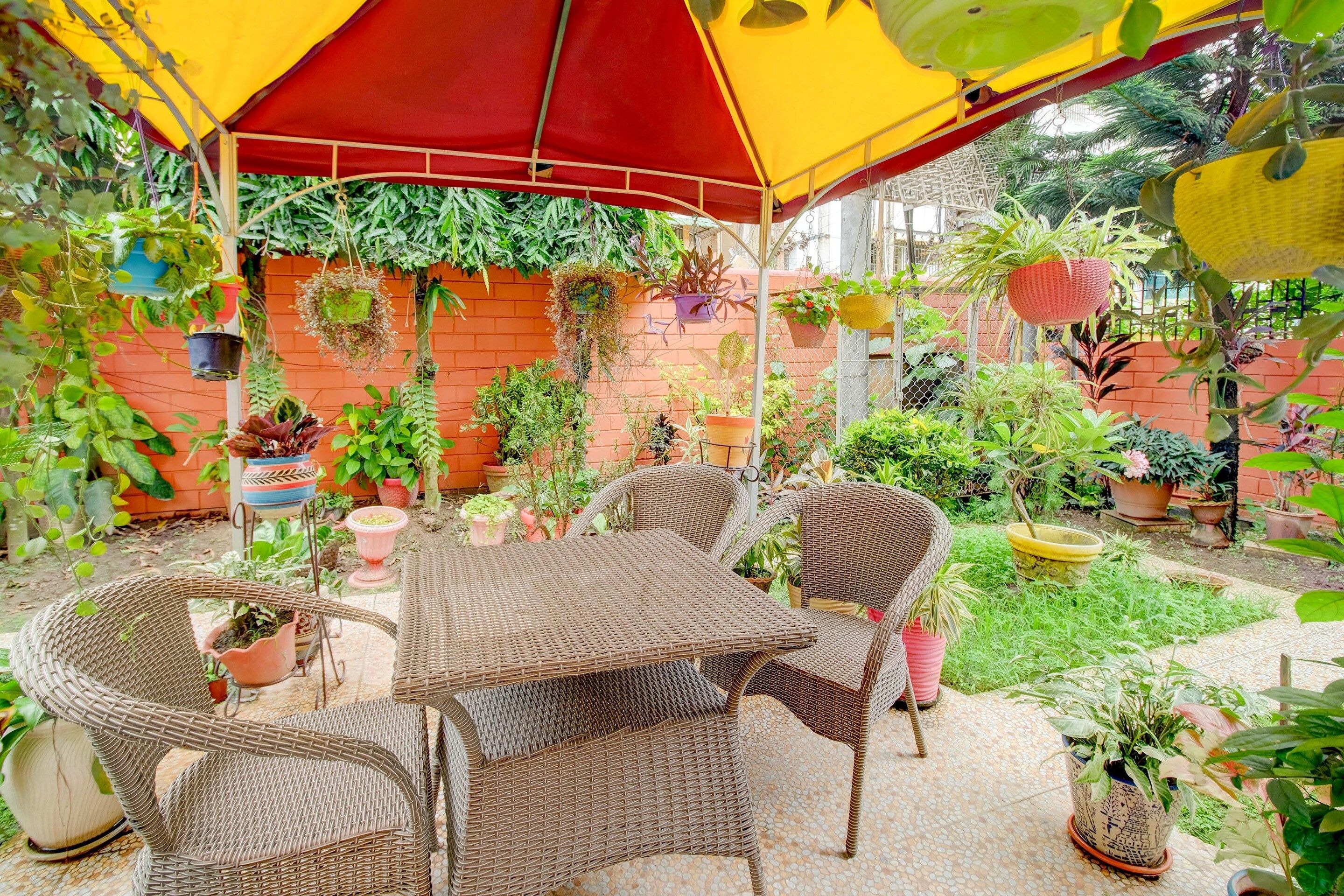 Un espace extérieur aménagé en terrasse, avec des meubles en osier, des plantes en pot et un auvent rouge et jaune.