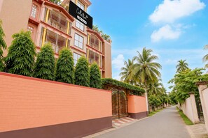 A multi-story building with a gated entrance, surrounded by lush greenery and palm trees. - Classic Cherry City Cottage (Guwahati)