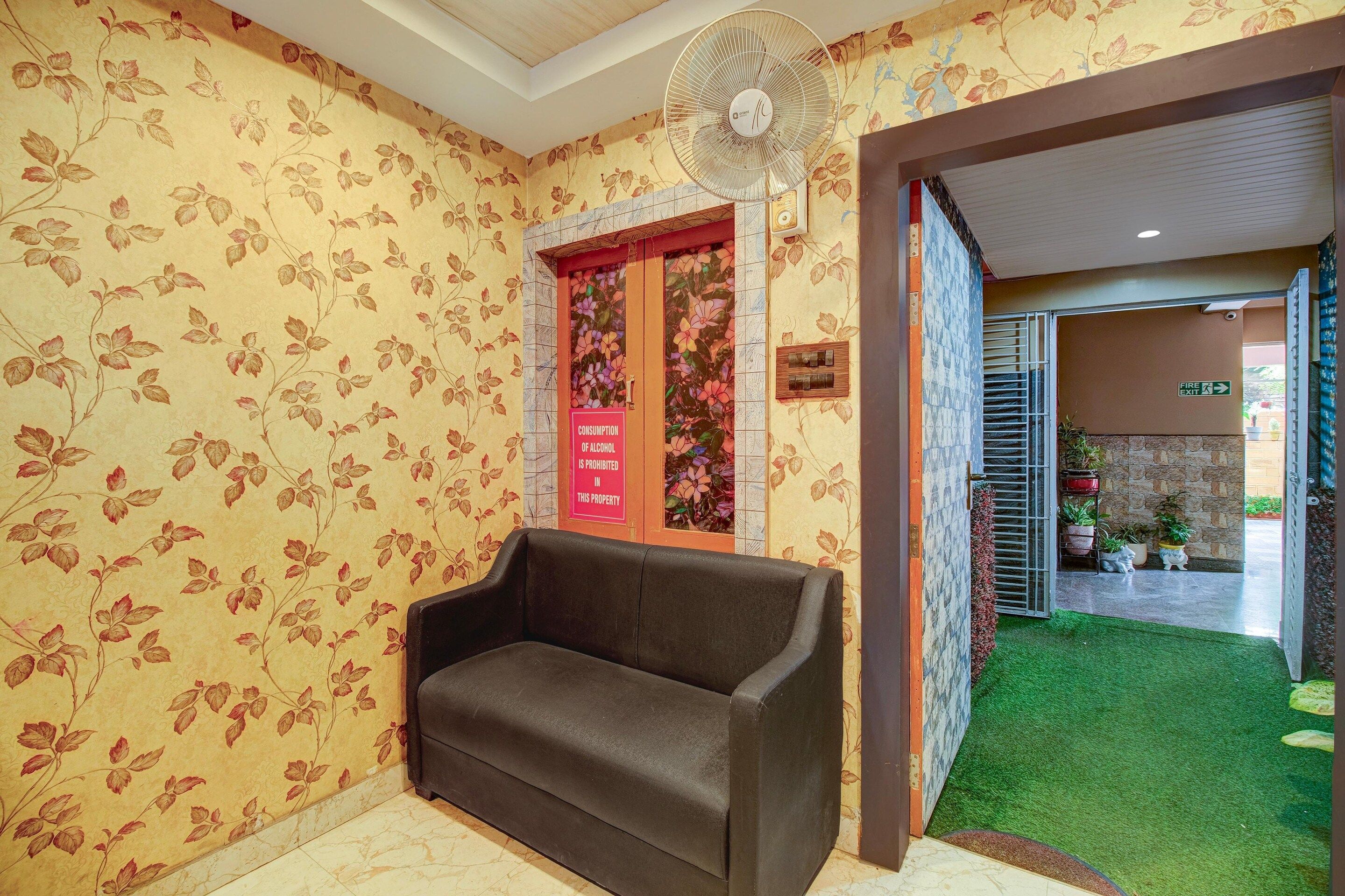 A reception area with a sofa, a fan, and a floral wallpaper.