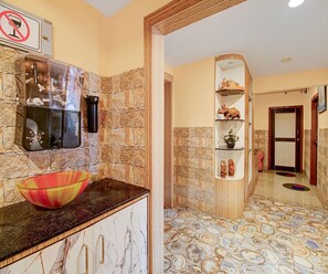 A kitchen with stone walls, a marble countertop, and a decorative shelf with items. - Classic Cherry City Cottage (Guwahati)