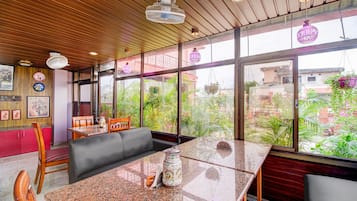 Una stanza con soffitto in legno, ampie finestre, un tavolo con sedie e vista sul verde circostante.