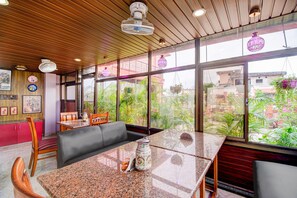 A room with a wooden ceiling, large windows, a table with chairs, and a view of greenery outside. - Classic Cherry City Cottage (Guwahati)
