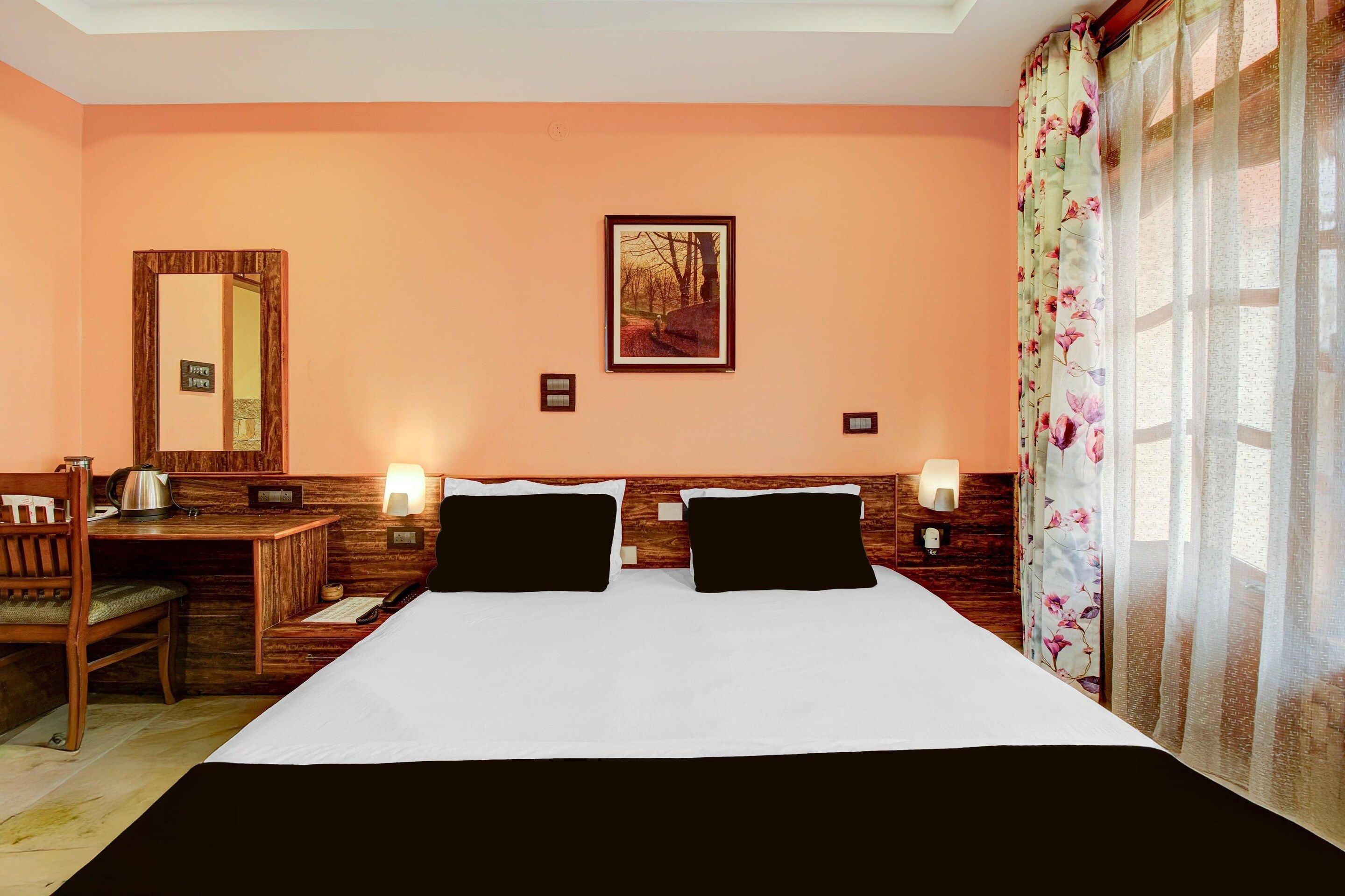 Una camera d'hotel con un letto, due comodini, una scrivania, una sedia, uno specchio e una finestra con tende.