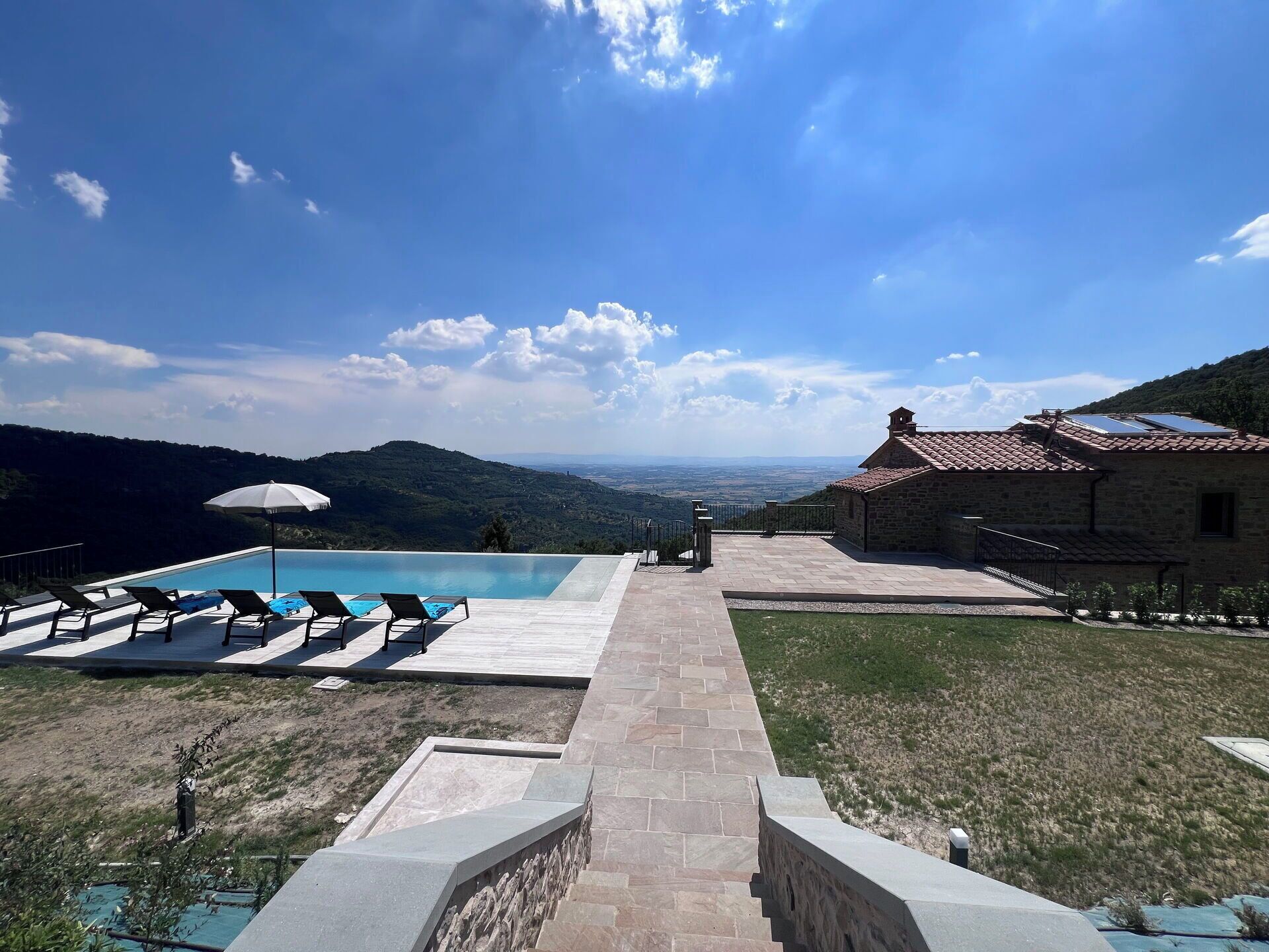 Una piscina con sillas de descanso, un sendero de piedra y vistas al paisaje.