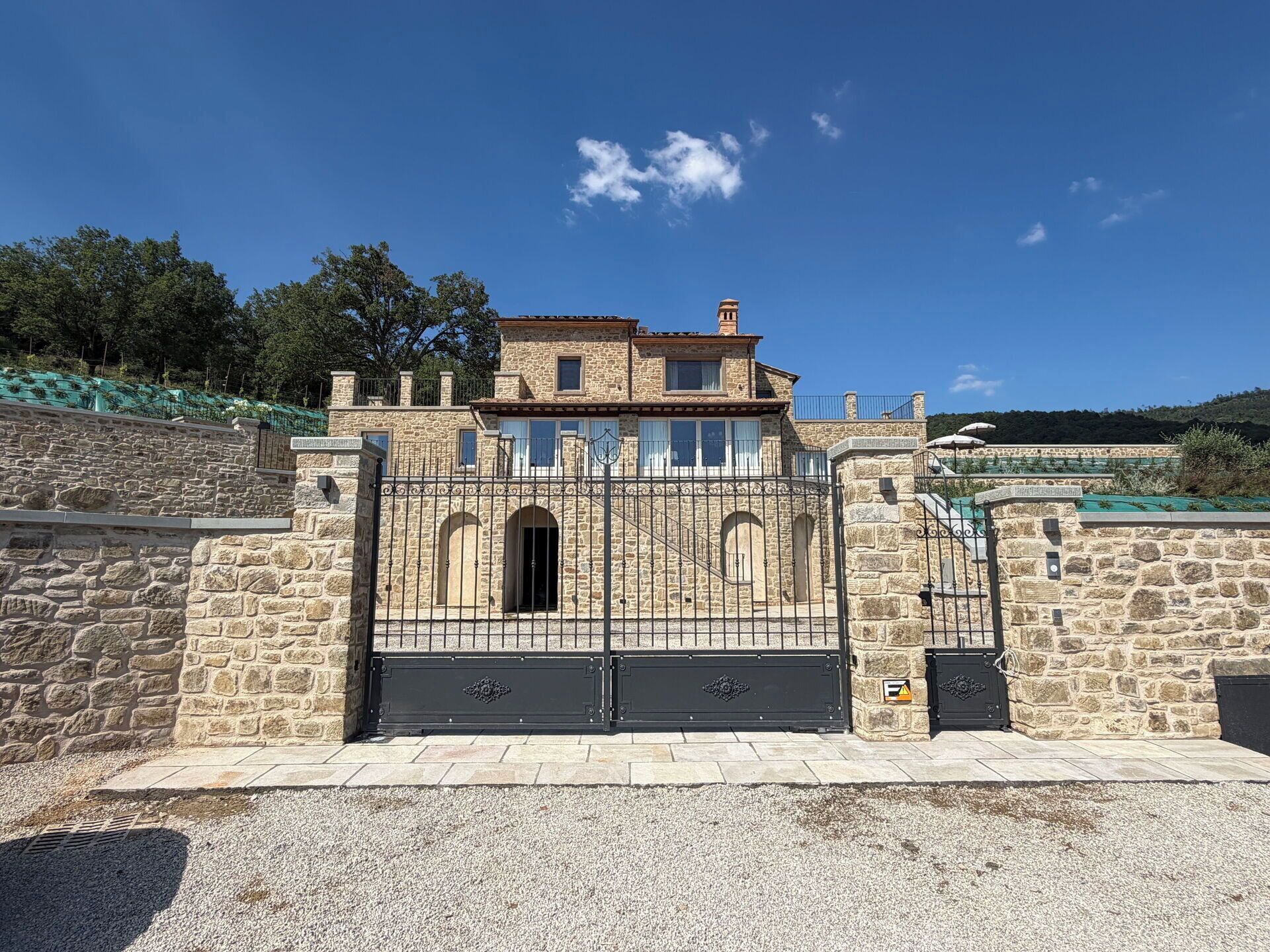 Un bâtiment en pierre doté d’une entrée fermée par un portail, d’un balcon et offrant une vue sur le paysage environnant.