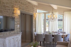 A dining area with a stone wall, a flat-screen TV mounted above a cabinet, and a chandelier. - Wonderful private villa for 8 guests with private pool, WIFI, A/C, patio and panoramic view (Cortona)