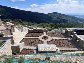 Ein Innenhof mit Steinmauern, einem zentralen Rundgarten und Blick auf ferne Berge.