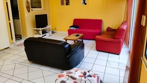 Ein Wohnzimmer mit einer schwarzen Couch, einer roten Couch, einem Couchtisch und einem Fernseher.