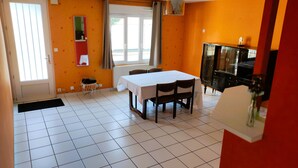 Ein Essbereich mit Tisch und Stühlen, eine Küche mit Kühlschrank und ein Fenster mit Vorhängen.