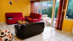 Ein Zimmer mit einer gelben Wand, einem roten Sofa, einem schwarzen Sofa, einem kleinen Holztisch und einem gemusterten Sitzsack.