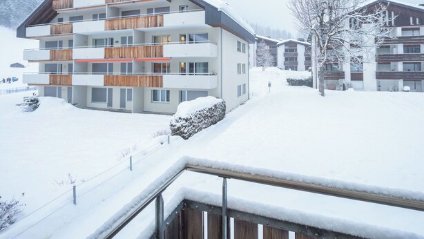 Ein mehrstöckiges Hotel mit Balkonen, einer verschneiten Landschaft und einem Bergpanorama.