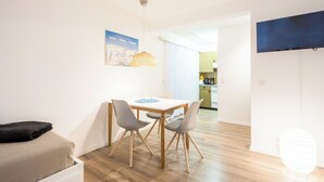 Ein modernes Zimmer mit Esstisch, zwei Stühlen, einer Couch und einer Küche im Hintergrund.