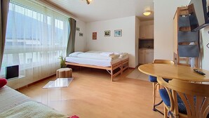 Una habitación de hotel con cama, una pequeña kitchenette, una mesa de comedor con sillas y un televisor.