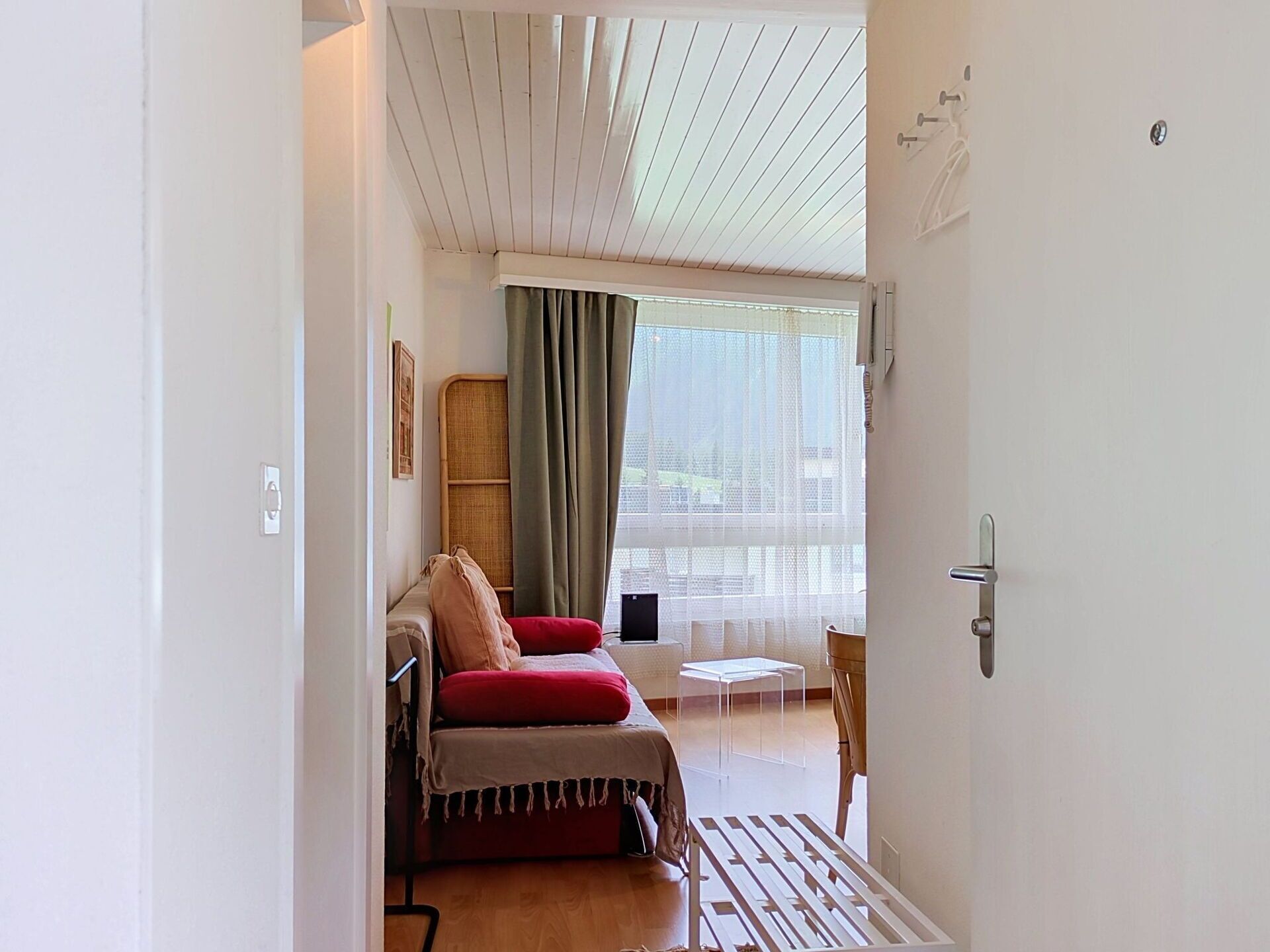 Ein Zimmer mit einem Bett, einem kleinen Tisch, einem Stuhl, einem Fenster mit Vorhängen und einer Tür.