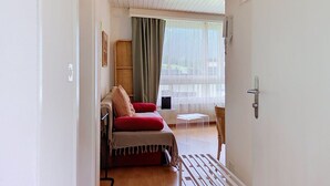 Una habitación con cama, una mesita, una silla, una ventana con cortinas y una puerta.