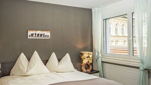 Una camera da letto con un letto, un comodino, una lampada, una finestra con tende e un quadro appeso al muro.