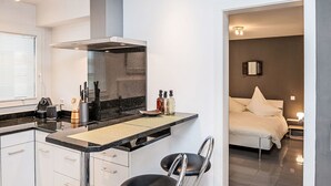 Una cucina moderna con piano cottura integrato, un piccolo angolo ristoro e vista su una camera da letto con letto e comodino.