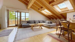Ein Loft-Zimmer mit Holzbalkendecke, einer Couch, einem Esstisch und Stühlen.