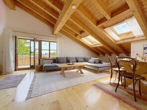 Avoin, loft-tyylinen huone, jossa on puinen kattopalkisto, sohva, ruokapöytä ja tuolit.