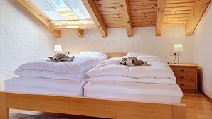 Ein Schlafzimmer mit Holzboden, einem Oberlicht, einem Bett mit weißer Bettwäsche, einem Nachttisch mit Lampe und einer kleinen Kommode.