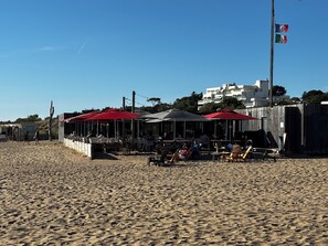 Un restaurante frente a la playa con terraza, cerca de una valla de madera y un asta de bandera.