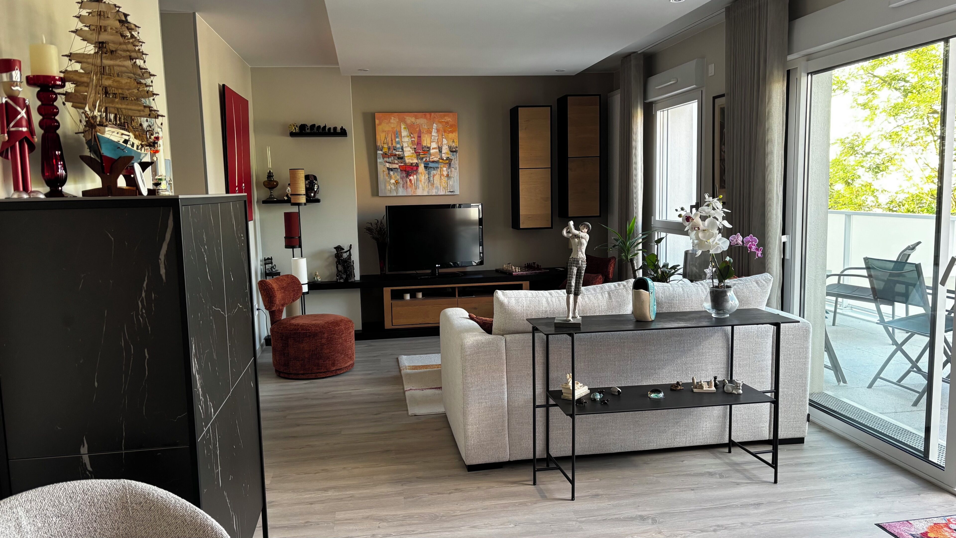 A modern living room with a TV, sofa, coffee table, and a balcony with outdoor furniture.