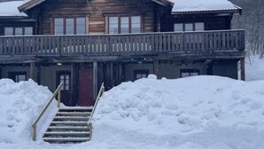En byggnad av trä med en balkong, en trappa som leder upp till entrén och snö som har samlats runt grunden.