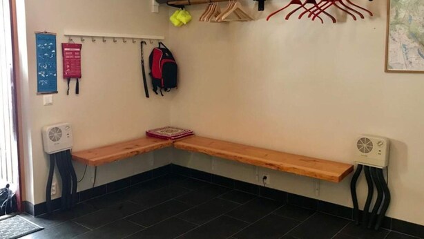 Ett hörnrum med en bänk, en klädhängare, en fläkt och en karta på väggen.