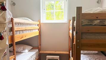 Habitación con literas, una pequeña banqueta y un enchufe en la pared.