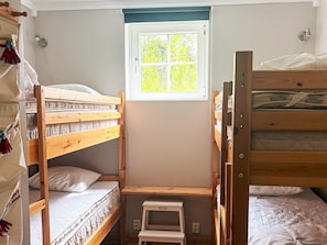 A bunk bed room with a window, a small step stool, and a wall-mounted outlet.