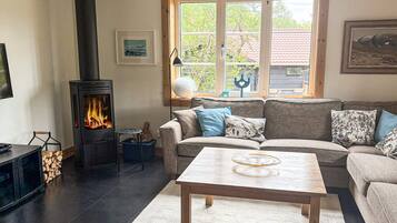 Una sala de estar acogedora con chimenea, un sofá, una mesa de centro y un ventanal con vistas a árboles y un edificio.