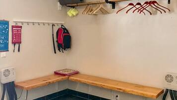 A corner room with a bench, a wall-mounted rack with hangers, a fan, and a small table.