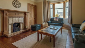 A living room with a fireplace, a sofa, a coffee table, and a view of the city through large windows. - Beautiful  villa for 8 guests with WIFI and TV (Lossiemouth)