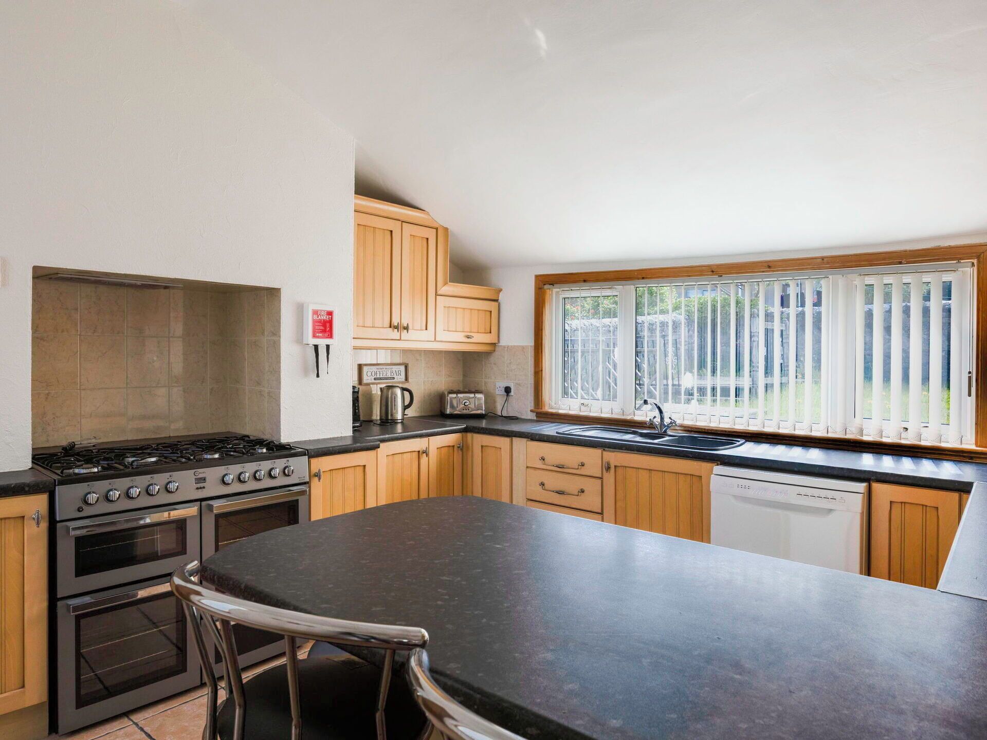 A kitchen with a gas stove, oven, coffee bar sign, and a window with blinds.
