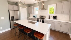 Een moderne keuken met een centraal eiland, barkrukken, roestvrijstalen apparatuur en een raam met uitzicht.