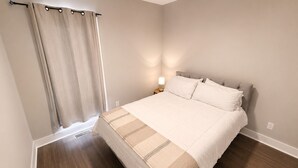 Een slaapkamer met een bed, nachtkastje, lamp, raam met gordijnen en een plafondventilator.