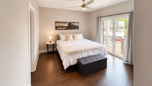 Een slaapkamer met een bed, een nachtkastje, een vloerlamp, een plafondventilator en een groot raam met uitzicht.