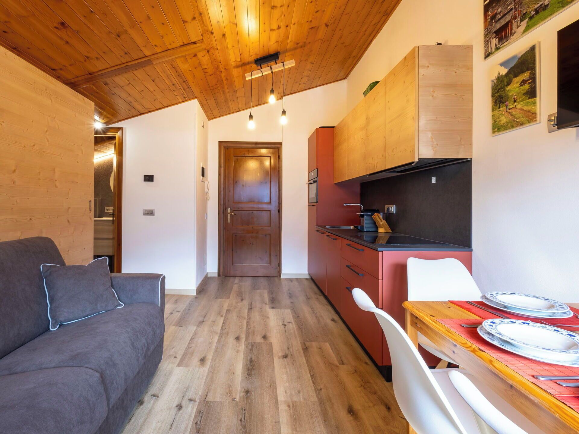 Un espace de vie compact doté d’un plafond en bois, d’une kitchenette, d’un coin repas avec une table et des chaises, et d’un canapé.
