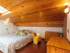 Ein Schlafzimmer mit Holzbalkendecke, einem Bett mit gemusterten Betttextilien, einer Nachttischlampe und einem Holzschrank.