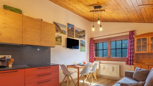 Eine moderne Küche mit Holzausstattung, eine Essecke mit Tisch und Stühlen, eine Sitzecke mit Sofa und ein Fenster mit Vorhängen.
