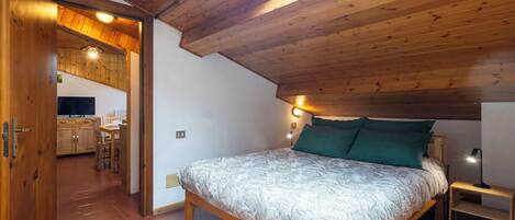 A bedroom with a skylight, wooden ceiling, and a bed with a patterned blanket.
