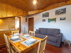 Ein Holzinterieur mit einem für vier Personen gedeckten Esstisch, einem grauen Sofa und Berglandschaftsbildern an der Wand.
