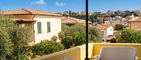 A terrace with outdoor furniture, a view of a hillside town, and a building with green shutters.
