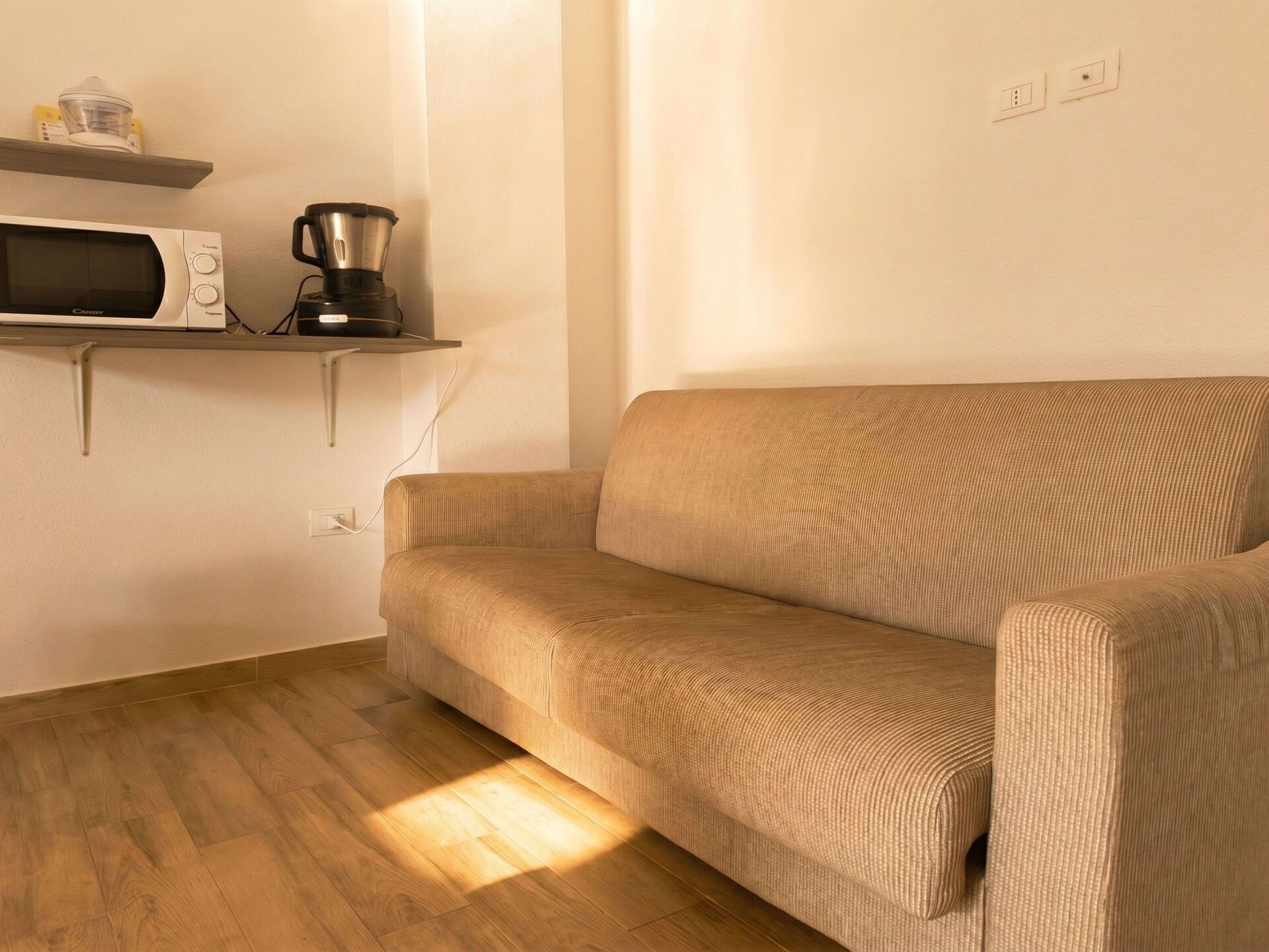 Ein Wohnzimmer mit einer Couch, einer Mikrowelle und einer Kaffeemaschine auf einem Regal.