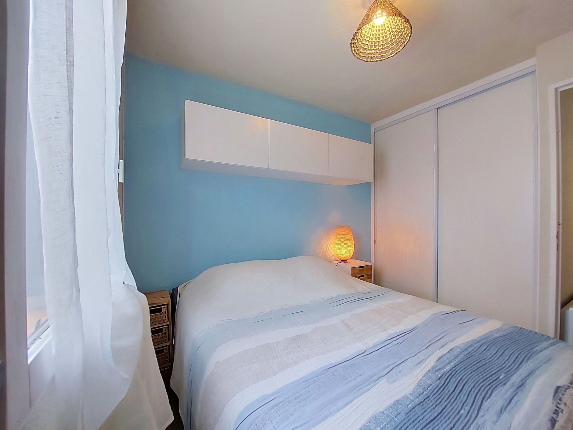 A bedroom with a bed, a bedside lamp, a wardrobe, and a hanging light fixture.