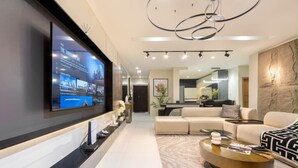 Un salon moderne doté d’un grand téléviseur à écran plat fixé au mur, d’un canapé d’angle, d’une table basse et d’un style de décoration minimaliste.