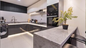 Une cuisine moderne équipée d’un lave-linge intégré, d’un four à micro-ondes et agrémentée d’une plante en pot.