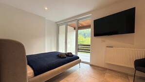 A bedroom with a bed, a television, a radiator, and a sliding glass door leading to an outdoor area.