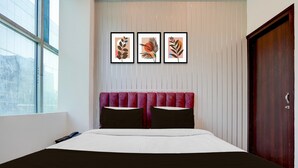 A hotel room with a bed, a window, a door, and three framed artworks on the wall. - Classic Gomti Nagar Station (Lucknow)