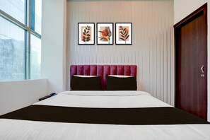Ein Hotelzimmer mit einem Bett, einem Fenster, einer Tür und drei gerahmten Kunstwerken an der Wand.